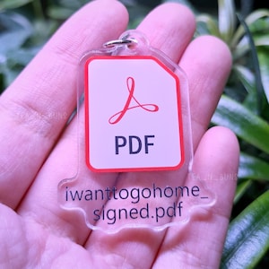 May include: A clear acrylic keychain shaped like a PDF file icon. The icon is red with a white background and the text "PDF" in black. The keychain has the text "iwanttogohome_signed.pdf" in black.