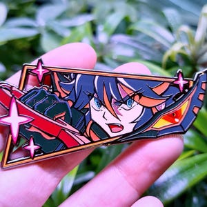 以下が含まれることがあります： 濃い青色の髪にオレンジ色のハイライトが入ったアニメキャラクターが赤い刃物を持っている、長方形のエナメルピン。黒いフレームにピンクの星のアクセントと鋭い角張ったラインが施されており、キャラクターの決意に満ちた表情が描かれています。