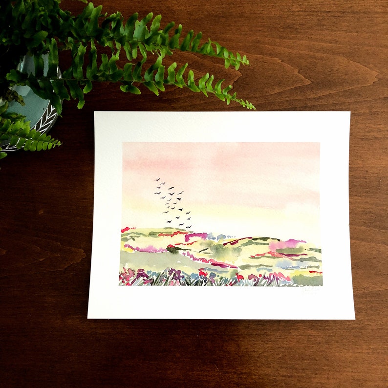 Puede incluir: Pintura acuarela de un paisaje con un cielo rosa, colinas verdes y una bandada de p&aacute;jaros volando en formaci&oacute;n. Las colinas est&aacute;n cubiertas de peque&ntilde;as flores rosas, moradas y amarillas.