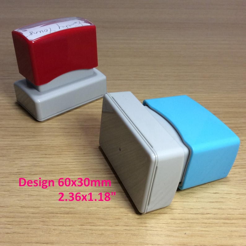 May include: Two rectangular self-inking stamps, one red and one blue. The red stamp has a white label with the text "(name) Stamp". The blue stamp has a white base. Design 60x30mm 2.36x1.18"