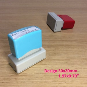 May include: A blue and white self-inking stamp with the text "1000 Happy Yours!" on a wooden surface. The stamp measures 1.97 inches by 0.79 inches.
