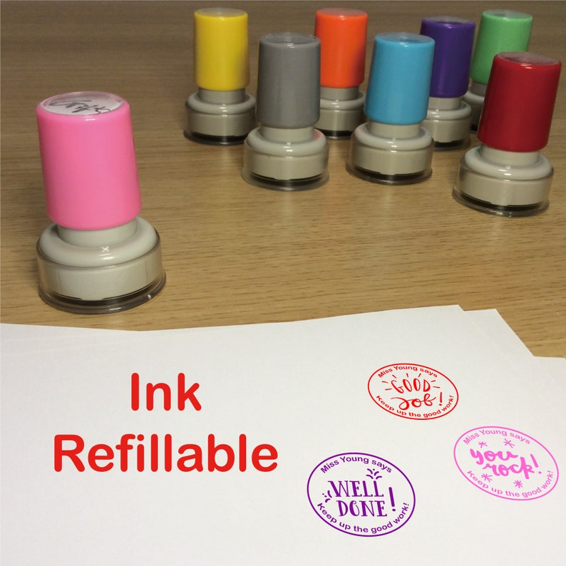 May include: A set of eight colorful ink stamps with a clear plastic base. The stamps are refillable and feature different messages, including "Good Job!" and "You Rock!" The stamps are on a wooden surface with a white sheet of paper.
