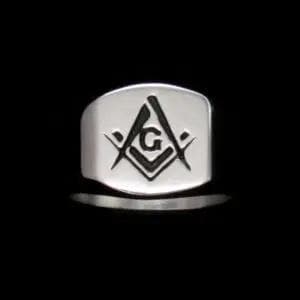 May include: A silver-colored ring with a rectangular face. The face of the ring features a black Masonic symbol, including a compass, square, and the letter "G". The ring is set against a black background.