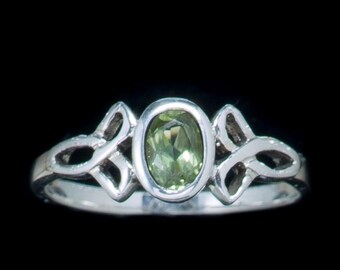 Può includere: Un anello d'argento con un designo a nodo celtico e una pietra preziosa ovale verde.