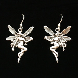 May include: A pair of silver earrings featuring a fairy design with wings and a flowing dress. The earrings are made of metal and have a dangling design.