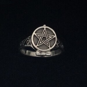Op de afbeelding: Een zilveren ring met een pentagram-ontwerp aan de bovenkant. Het pentagram bevindt zich in een rond, scharnierend compartiment.