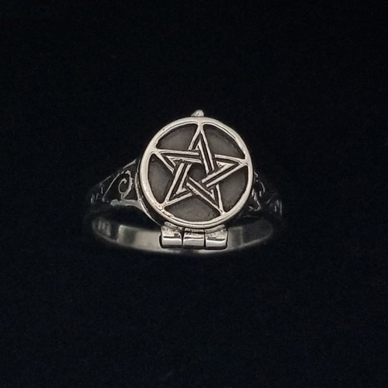 Op de afbeelding: Een zilveren ring met een pentagram-ontwerp aan de bovenkant. Het pentagram bevindt zich in een rond, scharnierend compartiment.