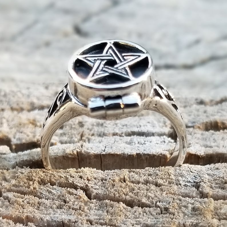 Op de afbeelding: Een zilveren ring met een scharnierend, rond medaillon met een pentagram-ontwerp. De ring is versierd en heeft een gedetailleerd ontwerp.