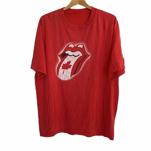 Op de afbeelding: Rood T-shirt met een witte afbeelding van het Rolling Stones tonglogo met een Canadees esdoornblad erin.