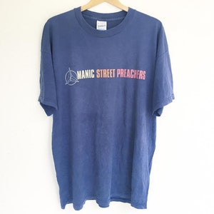 May include: A blue t-shirt with a white logo that says "Manic Street Preachers" in pink and orange lettering.