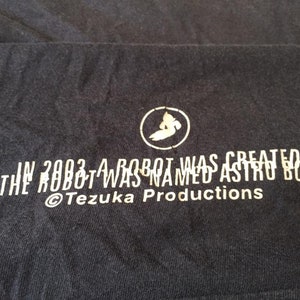 May include: A black t-shirt with white text that reads "In 2003 a robot was created. The robot was named Astro Boy. &copy;Tezuka Productions."