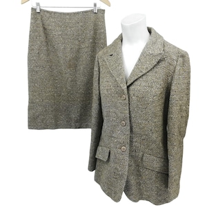 May include: A brown and white tweed skirt suit with a blazer and a skirt. The blazer has a notched collar, a button fastening, and a pocket on the left side. The skirt is knee-length and has a straight silhouette.