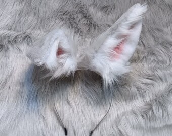 May include: White faux fur cat ears headband with a pink interior on a gray fuzzy background.