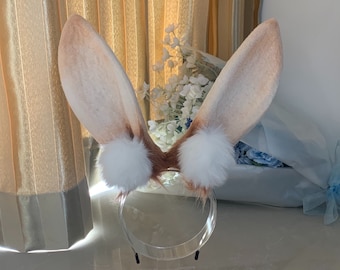 May include: A pair of brown bunny ears with white fur tips attached to a headband. The headband is clear plastic.