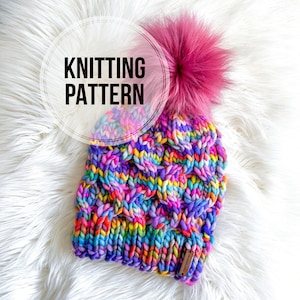 May include: A colorful knitted hat with a pink pom pom. The hat has a cable knit pattern and is made with a variety of colors, including purple, blue, green, yellow, orange, and red. The hat is sitting on a white fluffy surface. The text "Knitting Pattern" is written in a circle on the image.