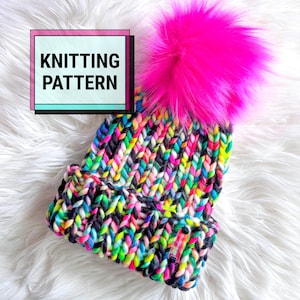 Peut inclure: Un bonnet en tricot épais avec un motif de fil multicolore vibrant composé de noir, rose fluo, jaune, bleu et blanc. Le bonnet possède un grand pompon en fausse fourrure rose vif sur le dessus et un revers avec une petite étiquette. Texte KNITTING PATTERN.