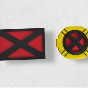 Può includere: Due disegni geometrici. Uno è un rettangolo nero con interno rosso e una X nera. L'altro è un cerchio giallo con centro rosso e una X nera. I disegni sono probabilmente legati a un fumetto o a un tema di supereroi.