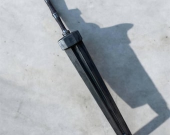 May include: A black sword with a silver hilt and a pointed tip. The sword is lying on a gray surface.
