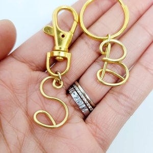 May include: Two gold keychains with the letters "S" and "B" made of wire. The keychains are attached to a gold key ring and a gold clasp.