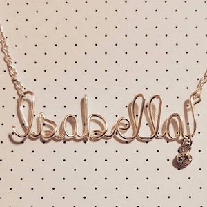 May include: A silver necklace with the name "Isabella" spelled out in wire. A small, clear crystal dangles from the end of the necklace.