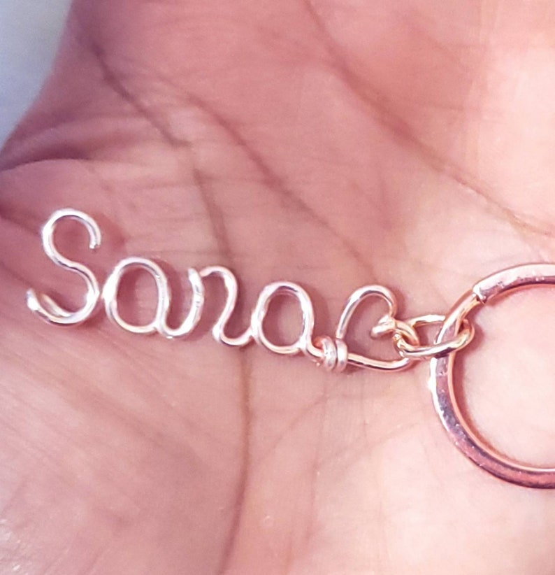 May include: A rose gold wire keychain with the name "Sara" and a heart charm.