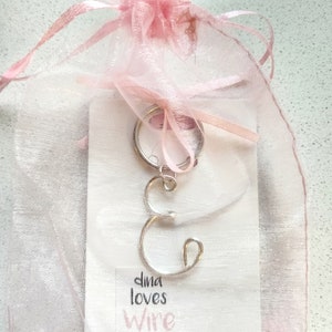 May include: A silver wire letter 'C' charm on a key ring, packaged in a pink organza bag. The card reads "dina loves wire" and "Dina Wire Home Jewelry & Accessories".