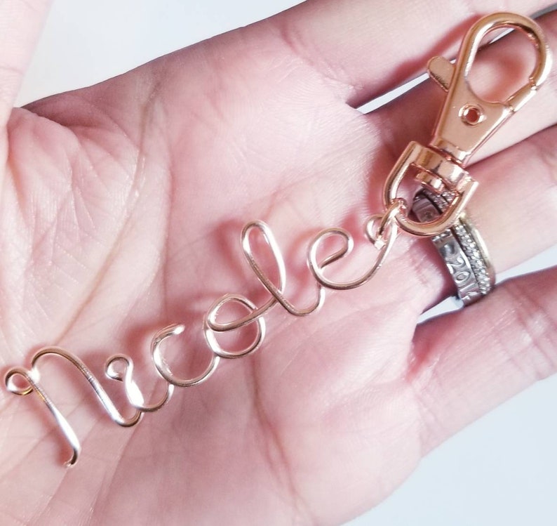 May include: Rose gold wire keychain with the name "Nicole" written in cursive.