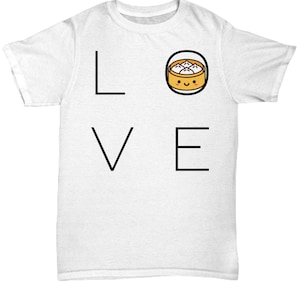 May include: White t-shirt with the word "LOVE" in black block letters. The "O" is replaced with a cartoon image of a dumpling in a bamboo steamer basket with a smiling face. A fun, food-themed graphic tee.