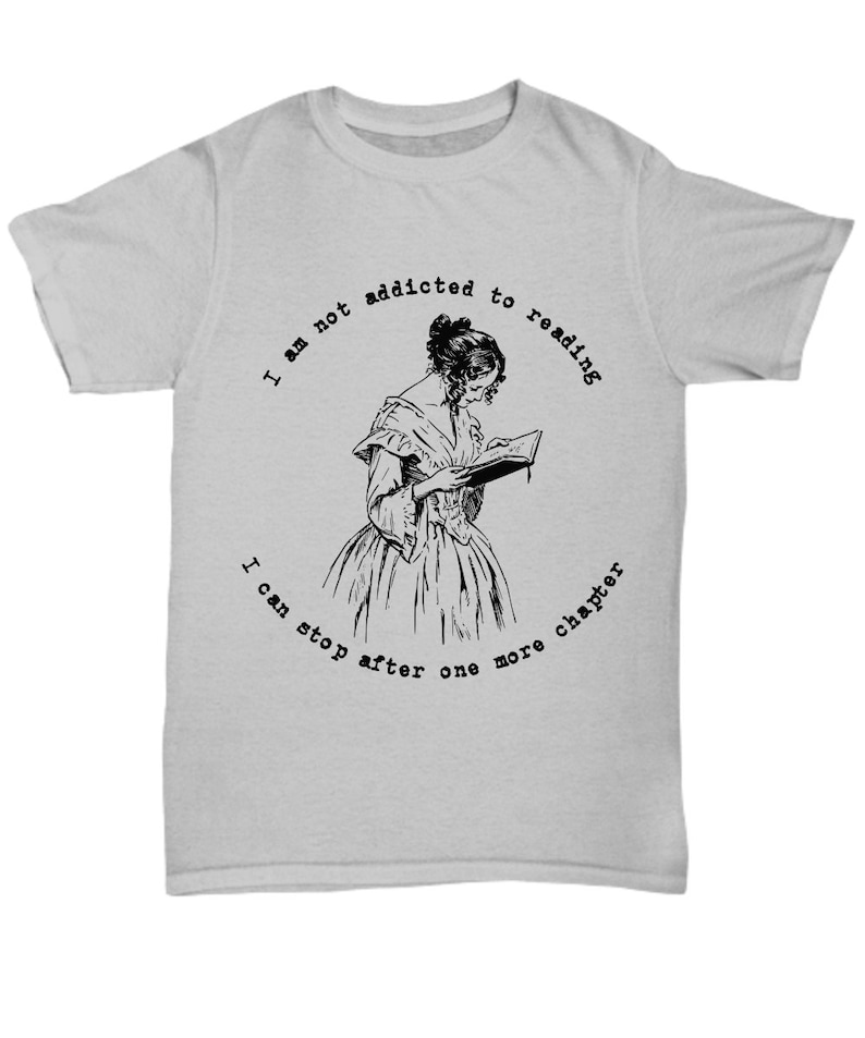 Peut inclure: T-shirt gris clair avec une illustration en noir et blanc d'une femme lisant un livre. Le texte autour de l'image dit : "Je ne suis pas accro &agrave; la lecture, je peux m'arr&ecirc;ter apr&egrave;s un autre chapitre."