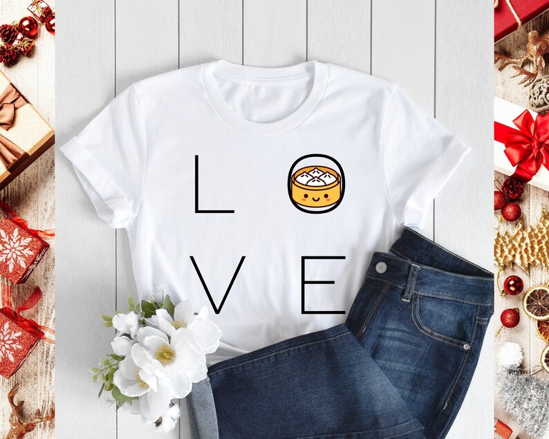 May include: White t-shirt with the word "LOVE" in black block letters. The "O" is replaced with a cartoon dumpling in a black circle. The shirt is paired with blue jeans. The image has a festive holiday theme.