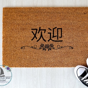 May include: A rectangular brown coir doormat with the Chinese characters for "Welcome" in black, above a floral design. Black and white sneakers are visible in the bottom right corner.