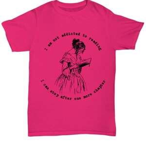 Peut inclure: T-shirt rose vif avec l'inscription "I am not addicted to reading, I can stop after one more chapter" entourant une illustration en noir et blanc d'une femme lisant. Le t-shirt est fait d'une mati&egrave;re douce.