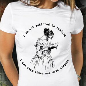 Peut inclure: T-shirt blanc avec un dessin noir d'une femme lisant un livre, entour&eacute; du texte "I am not addicted to reading, I can stop after one more chapter".