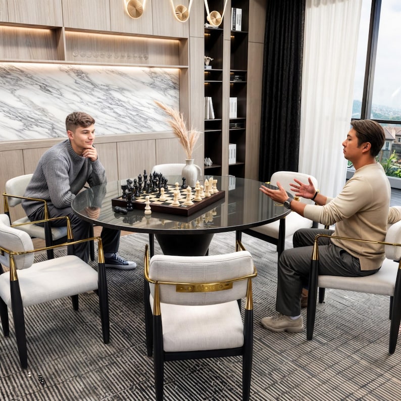 May include: Two people sit at a black glass table with a chessboard set in the center. The table has a black and gold modern design. The chairs are white with gold accents. The room has a modern design with a marble wall and a bookshelf.