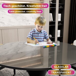 May include: A child sits at a round table with a clear protective cover, drawing on a piece of paper. The table is made of wood and has a black base. The text "Tisch gesch&uuml;tzt, Kreativit&auml;t frei!" and "Table protected, creativity free!" is visible in the image. The text "GLASKLAR TRANSPARENT" is also visible in the image.