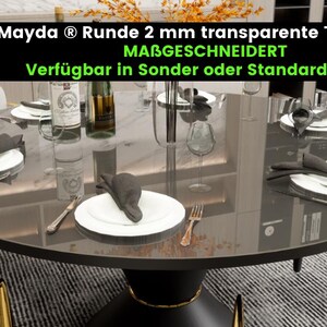 May include: A round black table with a glass top and gold legs. The table is set with white plates, black napkins, and silverware. The table is surrounded by chairs with gold legs. The text on the table reads "Mayda &reg; Runde 2 mm transparente Tischfolie MABGESCHNEIDERT Verf&uuml;gbar in Sonder oder Standardgr&ouml;&szlig;en".