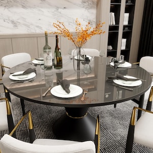 May include: A black round dining table with a glass top and a gold trim. The table is set with white plates, black napkins, and silverware. There are two bottles of wine on the table, and a vase of dried flowers in the center.