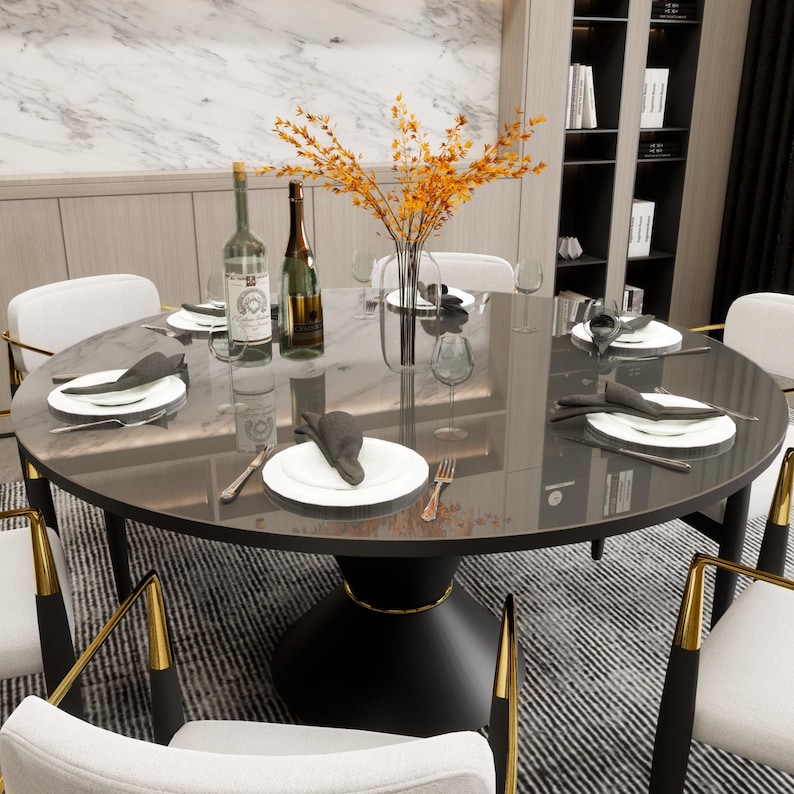 May include: A black round dining table with a glass top and a gold trim. The table is set with white plates, black napkins, and silverware. There are two bottles of wine on the table, and a vase of dried flowers in the center.