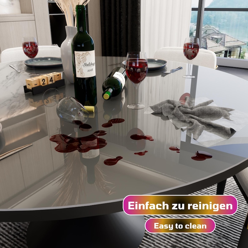 May include: A gray round table with a glass top. Red wine has been spilled on the table, and a cloth napkin is lying on the table. The text "Einfach zu reinigen" and "Easy to clean" is visible on the table.