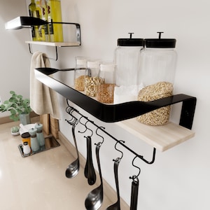 May include: Black metal wall-mounted shelf with a wooden top shelf and hooks underneath. The shelf is holding various glass jars and kitchen utensils.