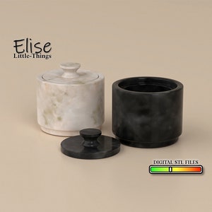 Puede incluir: Dos recipientes redondos de mármol con tapas. Un recipiente es blanco con un patrón de mármol verde y el otro es negro. Los recipientes están etiquetados como "Elise Little-Things".