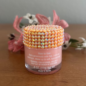 Puede incluir: Un peque&ntilde;o frasco transparente de tratamiento labial color melocot&oacute;n con una tapa cubierta de pedrer&iacute;a naranja iridiscente. La etiqueta dice: How to Use: Apply generously onto lips. Leave on overnight. Wake up to soft, hydrated lips! 17g Net Wt.