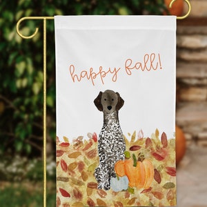 May include: A white garden flag with the text "happy fall!" in orange. A brown and white German Shorthaired Pointer dog sits in a pile of colorful autumn leaves with a pumpkin and a gourd.