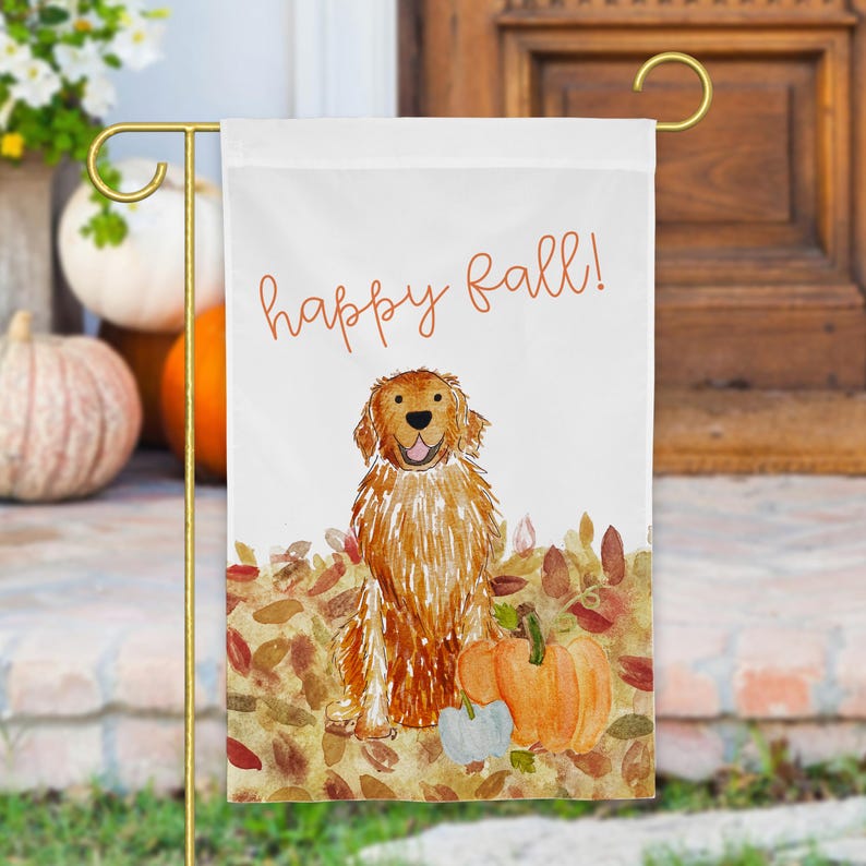 Pode incluir: Uma bandeira de jardim branca com uma ilustra&ccedil;&atilde;o em aguarela de um golden retriever sentado entre folhas de outono e ab&oacute;boras. O texto "happy fall!" est&aacute; escrito em letra cursiva laranja acima do c&atilde;o. A bandeira pende de um suporte de metal dourado.