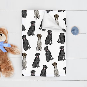 May include: A white baby blanket with a repeating pattern of black and white dogs. The dogs are in various poses, including sitting, standing, and running. The blanket is soft and cuddly, perfect for a baby's nursery.
