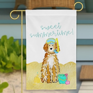 May include: A white garden flag featuring a watercolor illustration of a brown dog wearing a blue and yellow snorkel mask. The text "sweet summertime!" is printed in teal above the dog, which sits on a yellow sand base with a sandcastle and bucket.