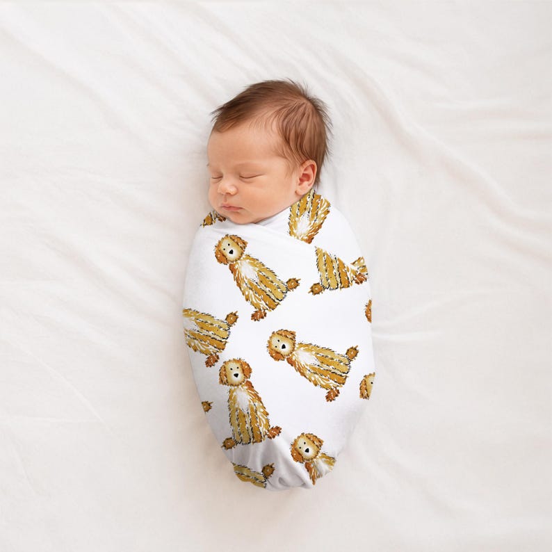 May include: A white swaddle blanket featuring a repeating pattern of illustrated golden-brown dogs with shaggy fur. The fabric is wrapped snugly around a sleeping infant, displaying the canine print clearly across the entire surface of the wrap.