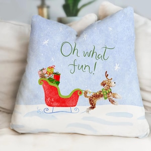May include: A square throw pillow with a light blue background featuring white snowflakes and the text Oh what fun! in green script. A brown dog with antlers pulls a red sleigh filled with colorful wrapped gifts across a white snowy surface.