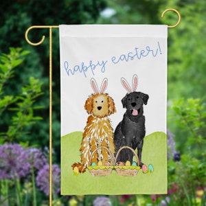 May include: A white garden flag with the text "happy easter!" in blue script. Two dogs, one brown and one black, are wearing bunny ears and holding baskets of colorful Easter eggs.