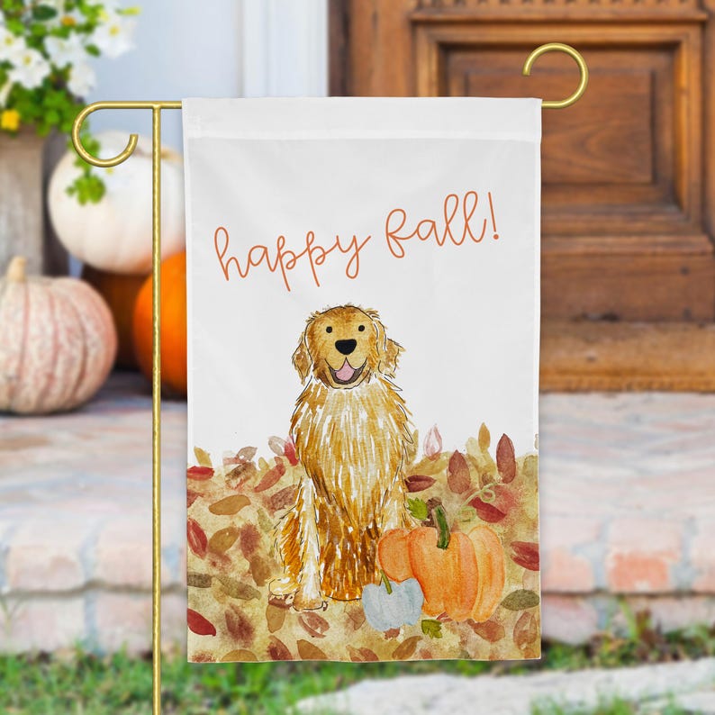 Pode incluir: Uma bandeira de jardim branca com uma ilustra&ccedil;&atilde;o em aguarela de um golden retriever sentado num monte de folhas de outono castanhas e cor de laranja com duas ab&oacute;boras. O texto "happy fall!" est&aacute; impresso em cursivo laranja acima do c&atilde;o.